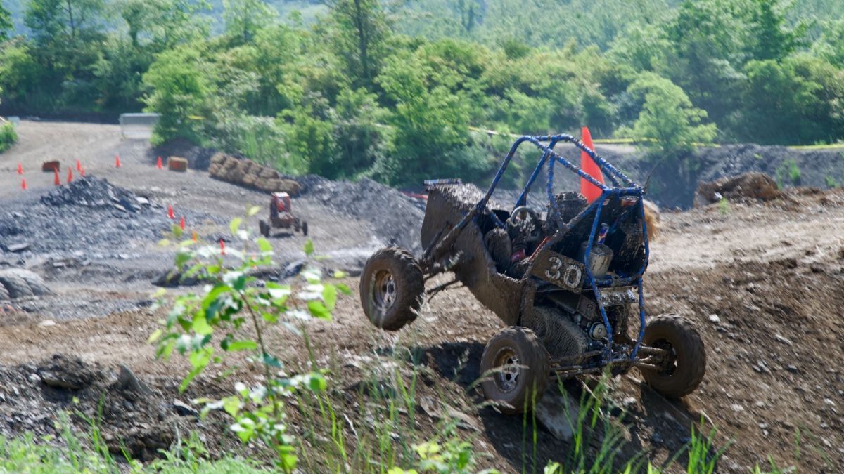 Photo of an off-road vehicle going over a muddy terrain, with green trees in the background