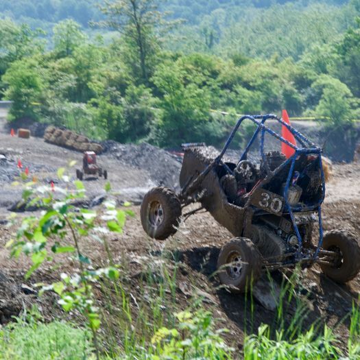 Photo of an off-road vehicle going over a muddy terrain, with green trees in the background