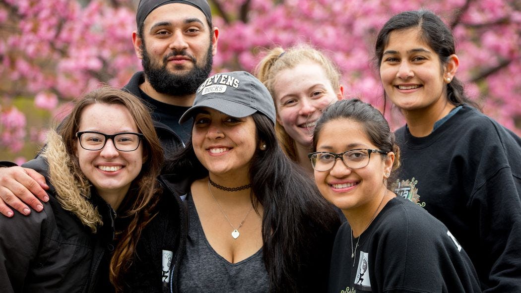 Six students smiling in front of trees with flowers