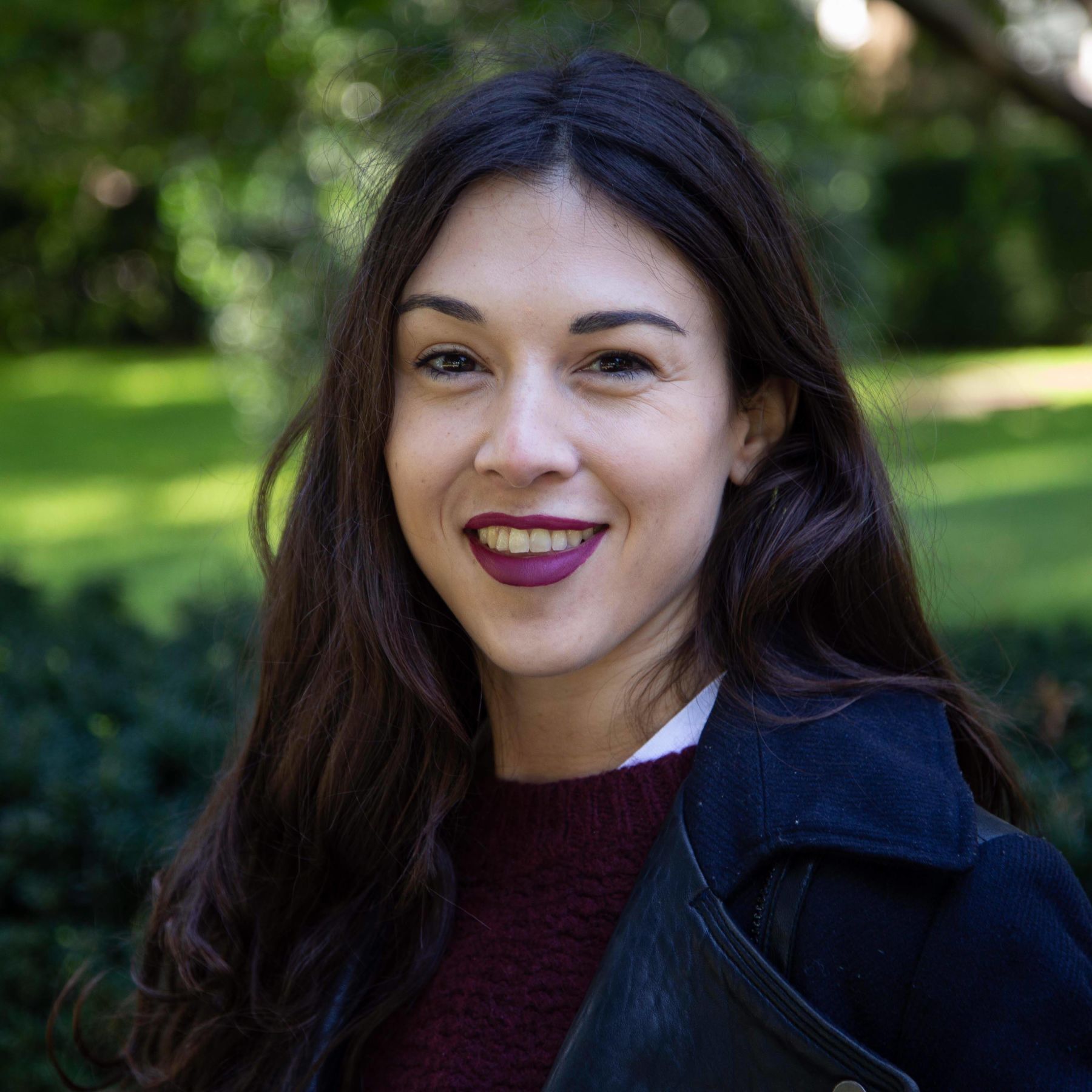 Head and shoulders portrait of Justine Herve with the hedges and a lawn as the background.