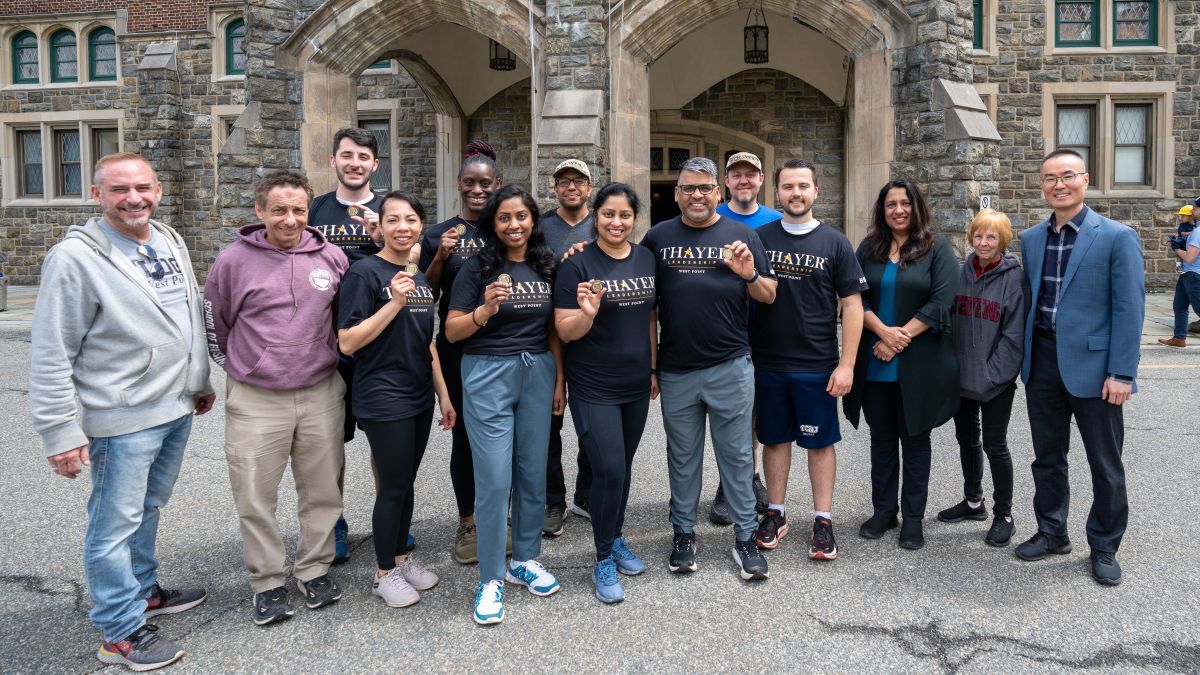 The EMBA cohort stands in front of the Thayer Hotel at West Point holding their Army coins.