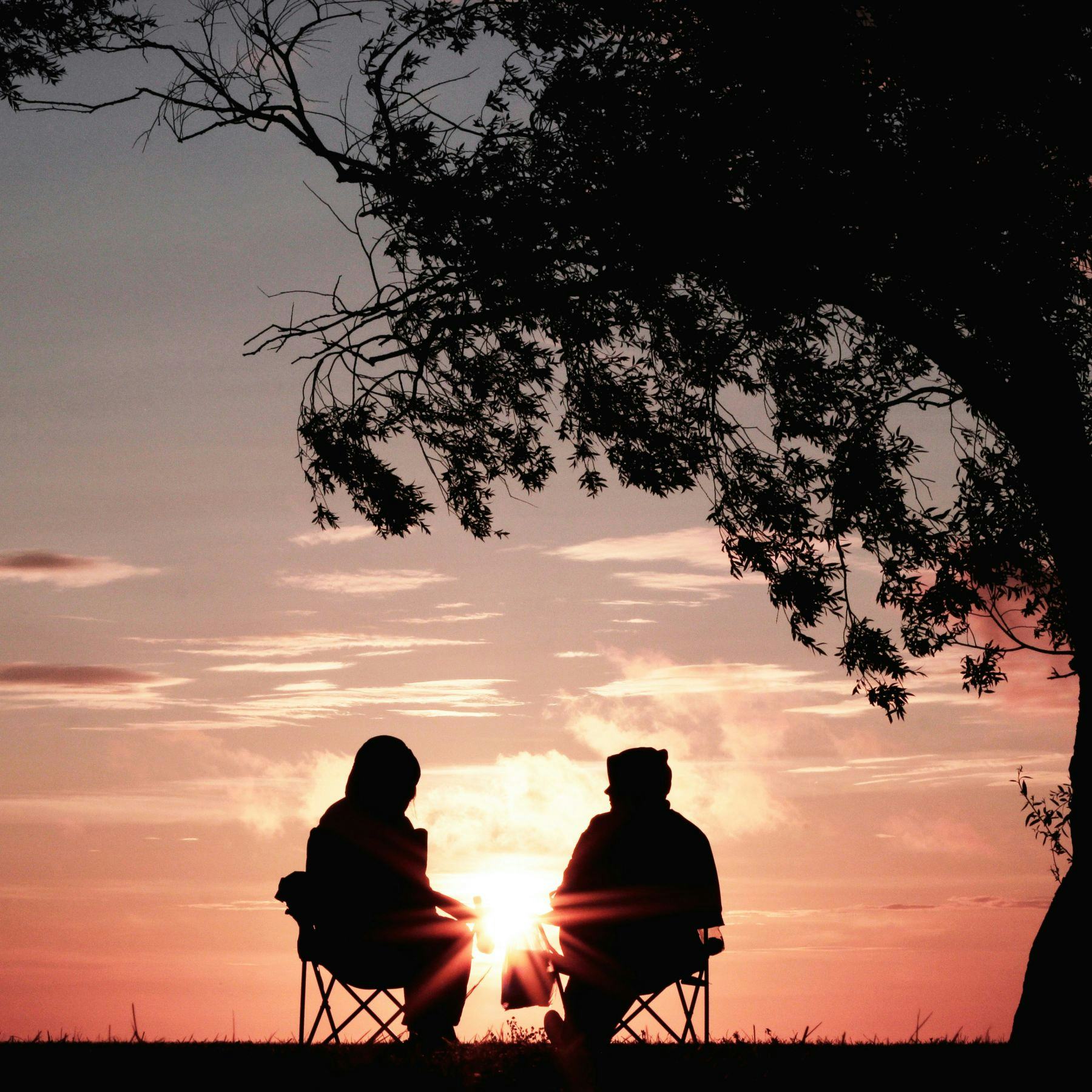 Two elderly people sitting in silhouette against sunset