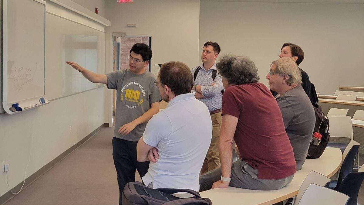 Six math educators look at a problem on a white board during a mathematics conference at Stevens.