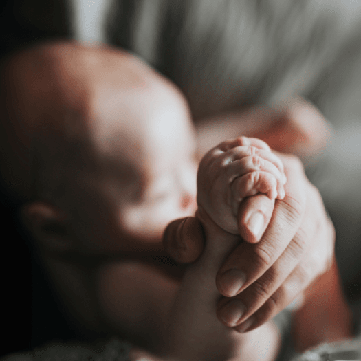 A newborn baby grasping the hand of an adult