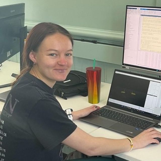 Photo of Samantha Gajda smiling at the camera while working on a computer