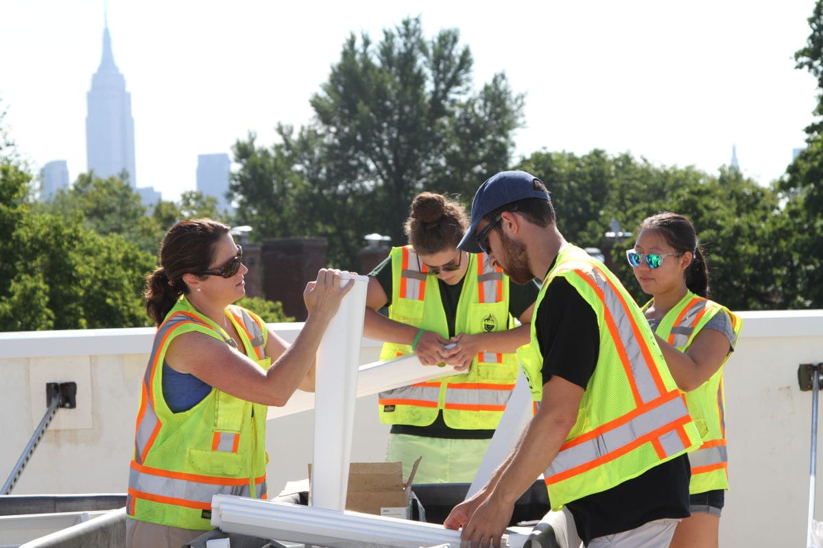 Faculty and students wearing safety vests working with building materials outdoors with the Empire State Building in the background.