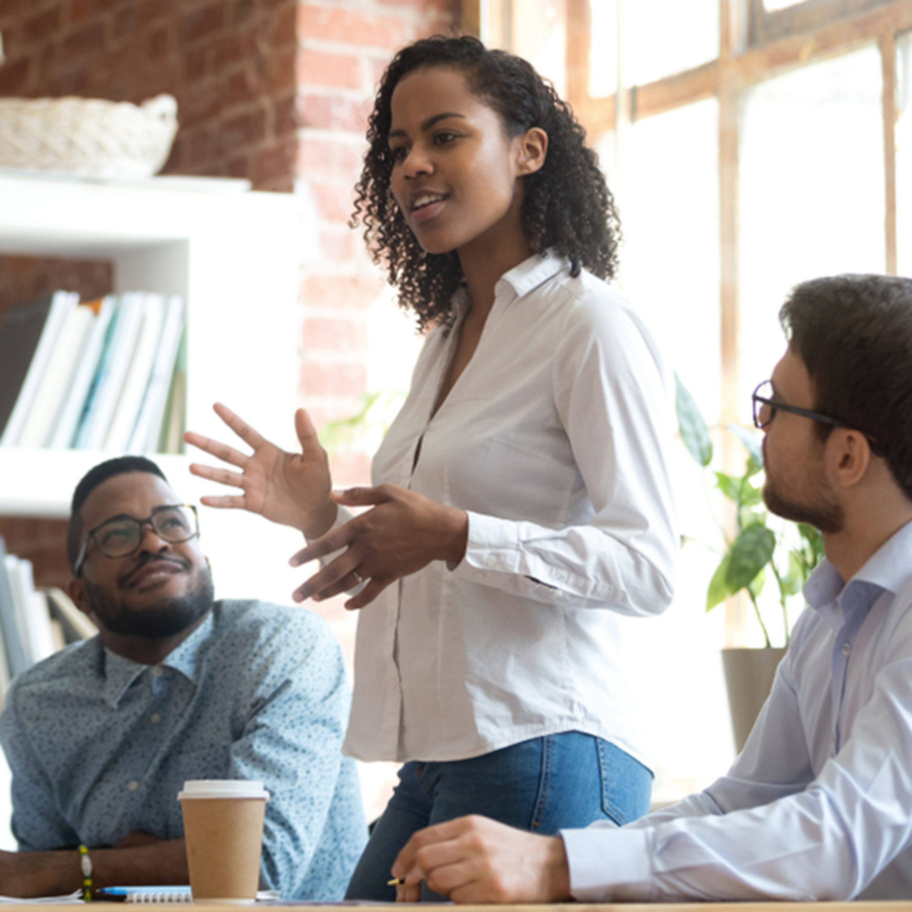 A women of color stands, addressing a group of diverse individuals around her.