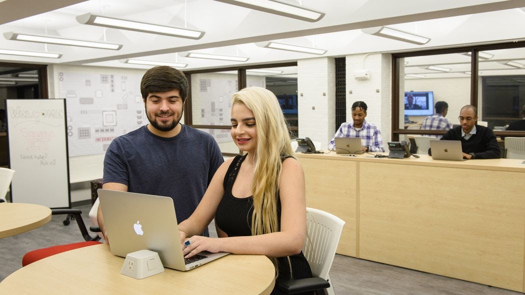 Two students looking at a laptop with IT staff in background