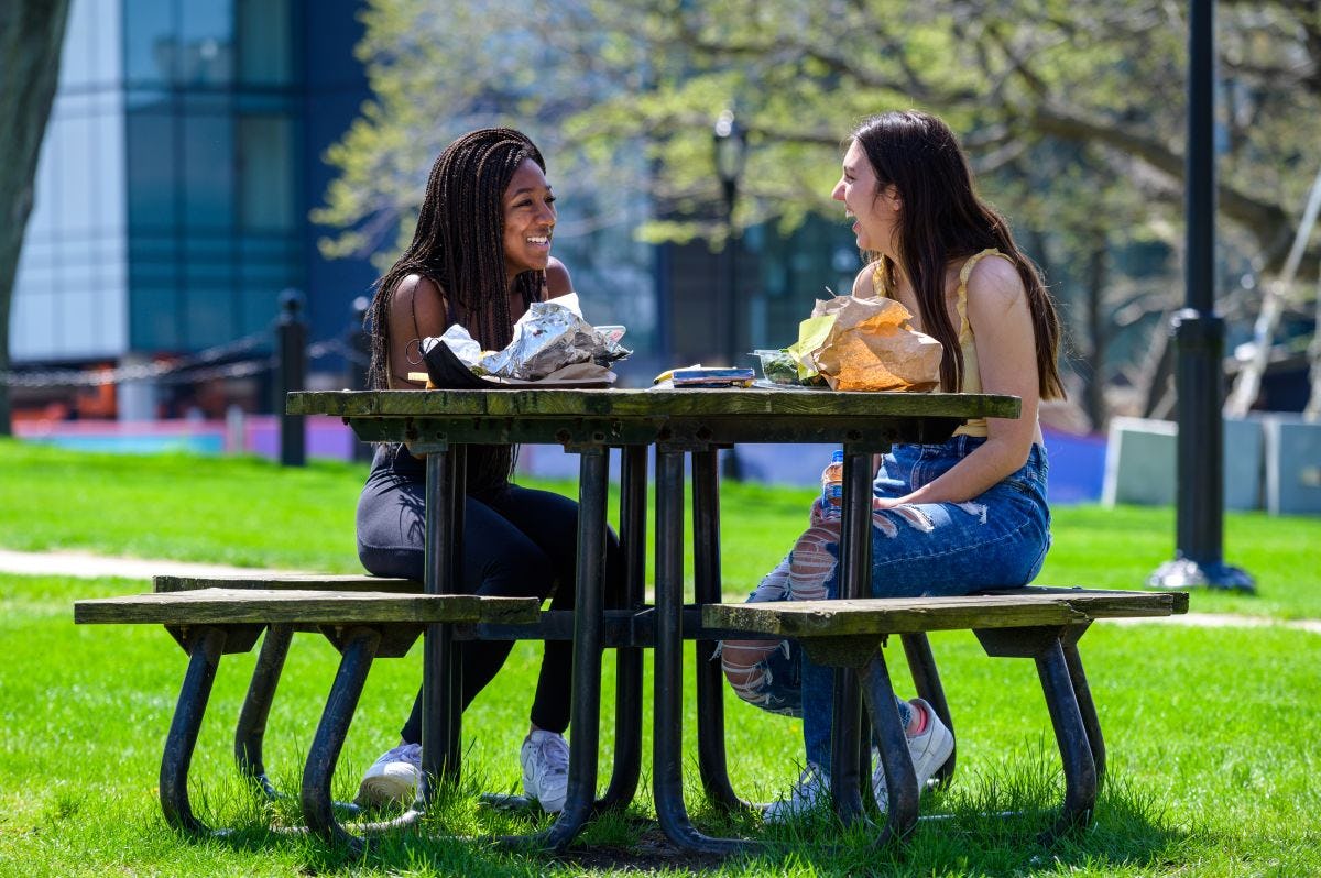 Two female students laugh outside on picnic table