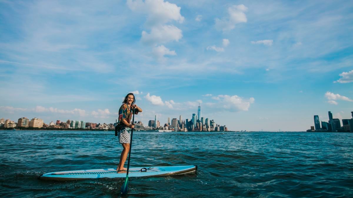 Jeremy Roche stand up paddle boarding on the Hudson River in front of the New York City skyline