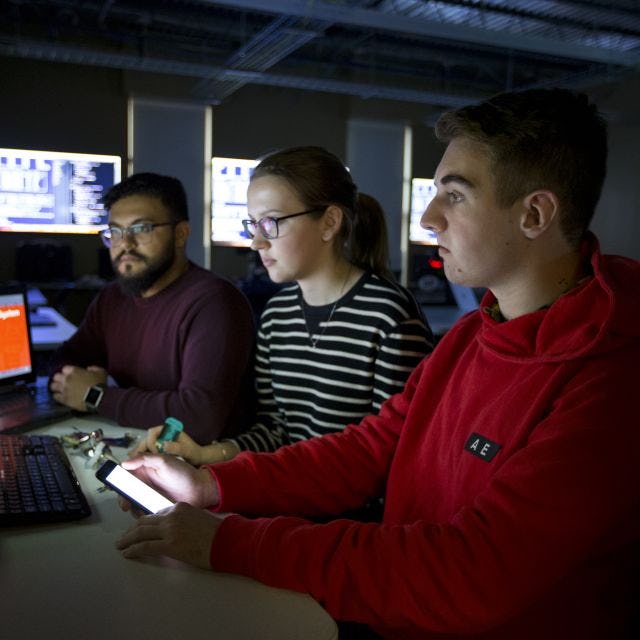 Three students looking at a laptop in dark room