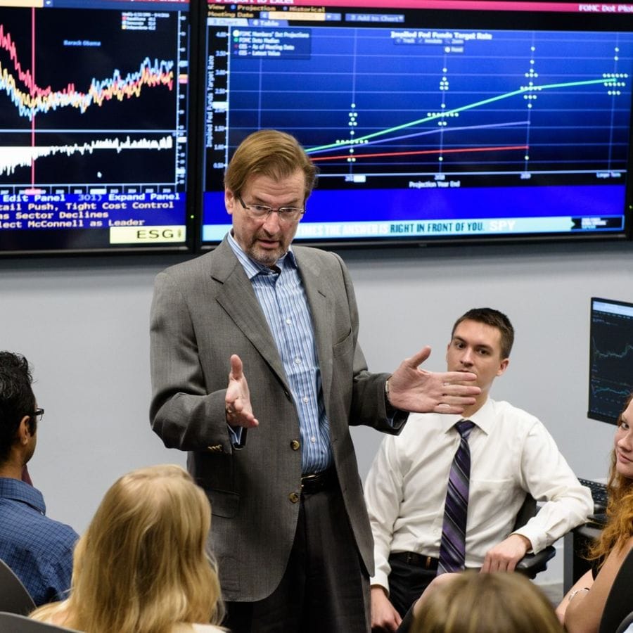 Students gather around professor in finance lab