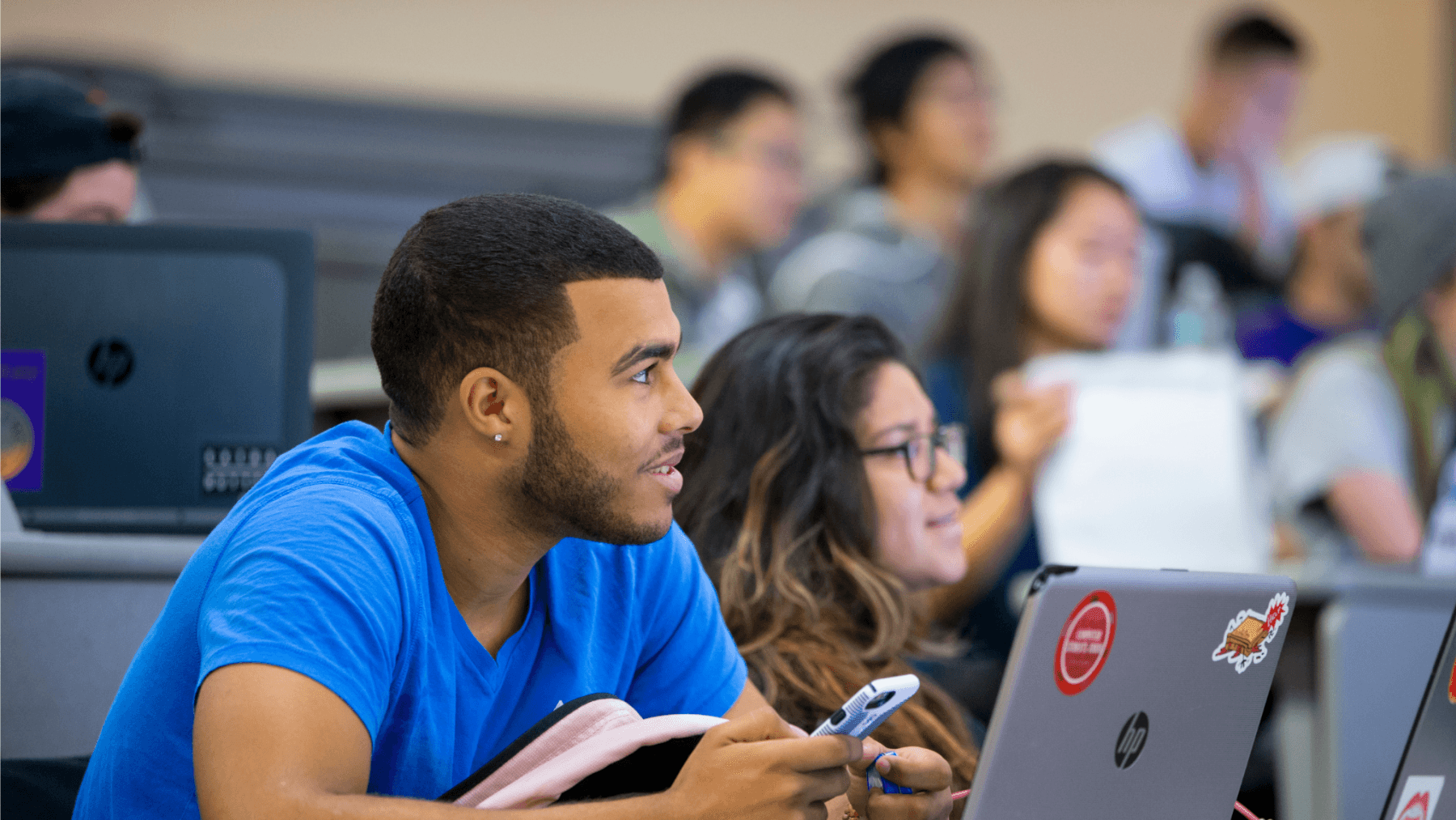 Two students of color looking at laptop computers from desks in a classroom