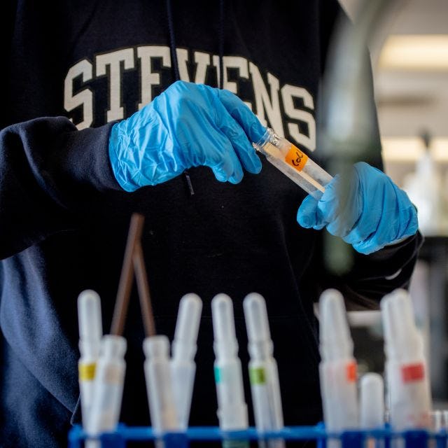 Student in a Stevens sweatshirt handling test tubes in a lab.