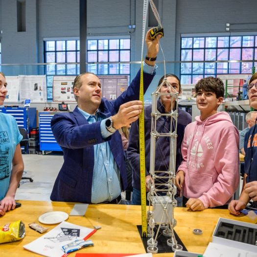 Photo of a man holding up a measuring tape to a tower while four students surround him looking up
