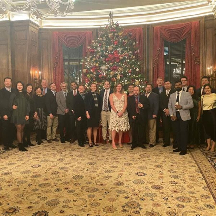 A group of alumni gather for a picture in front of the festive tree for the D.C. holiday party