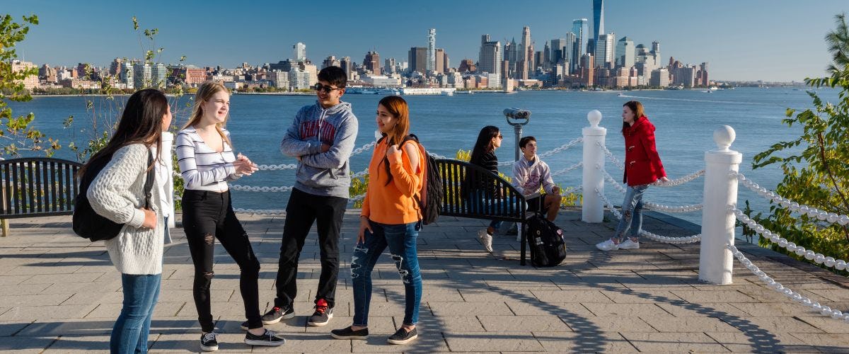 Students socialize at Castle Point with New York skyline in background.