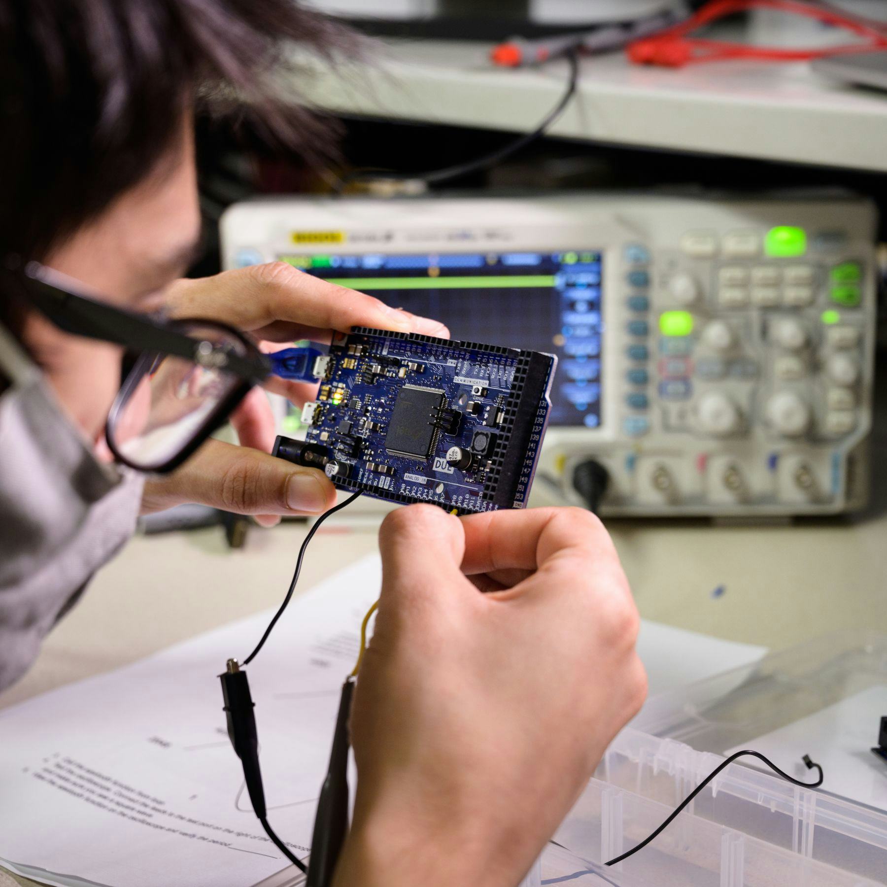 Student wearing glasses adjusts circuit board