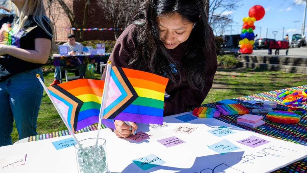 student signing a poster at the LGBTQ resource fair