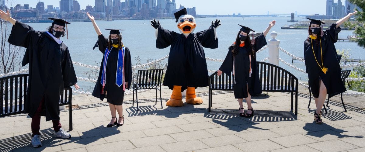 4 students and Attila in cap and gown with NYC skyline in background