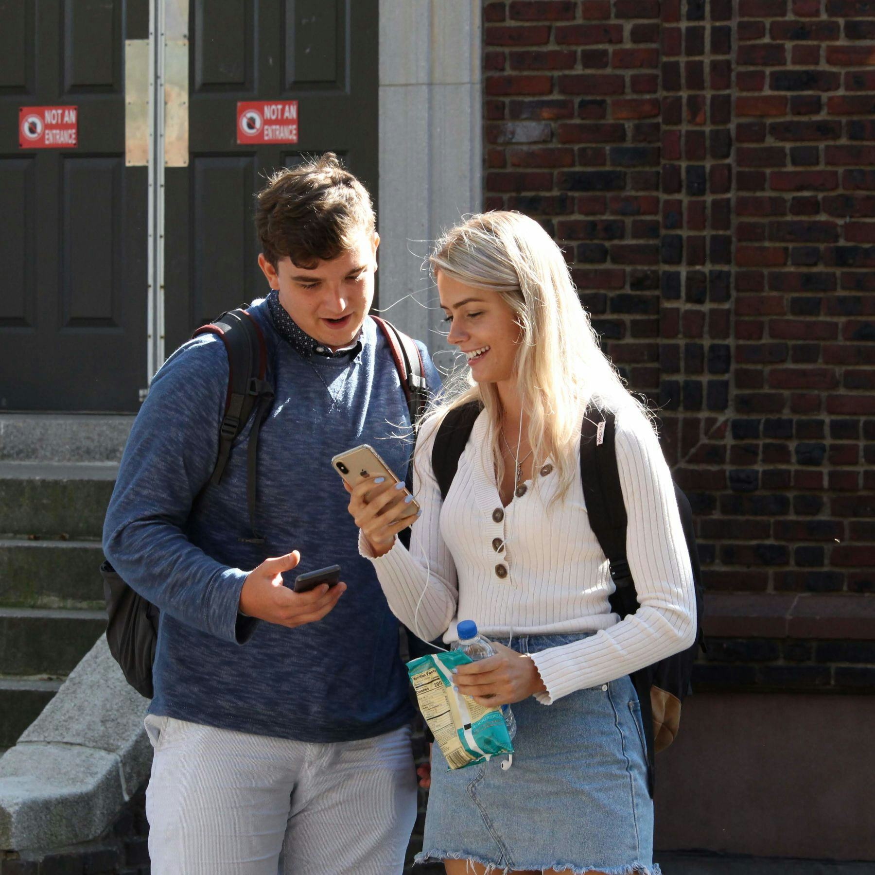 A male and female Stevens student smile looking at the women's smartphone.