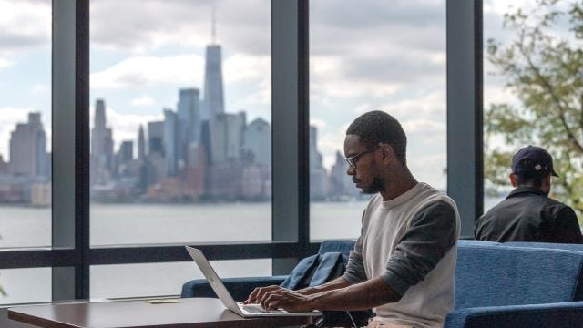 Student works on laptop in the UCC with New York city skyline in background.