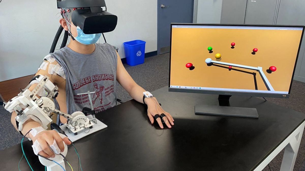 A person wearing a VR headset and arm brace equipped with sensors plays a computer game to improve coordination, strength and muscle control